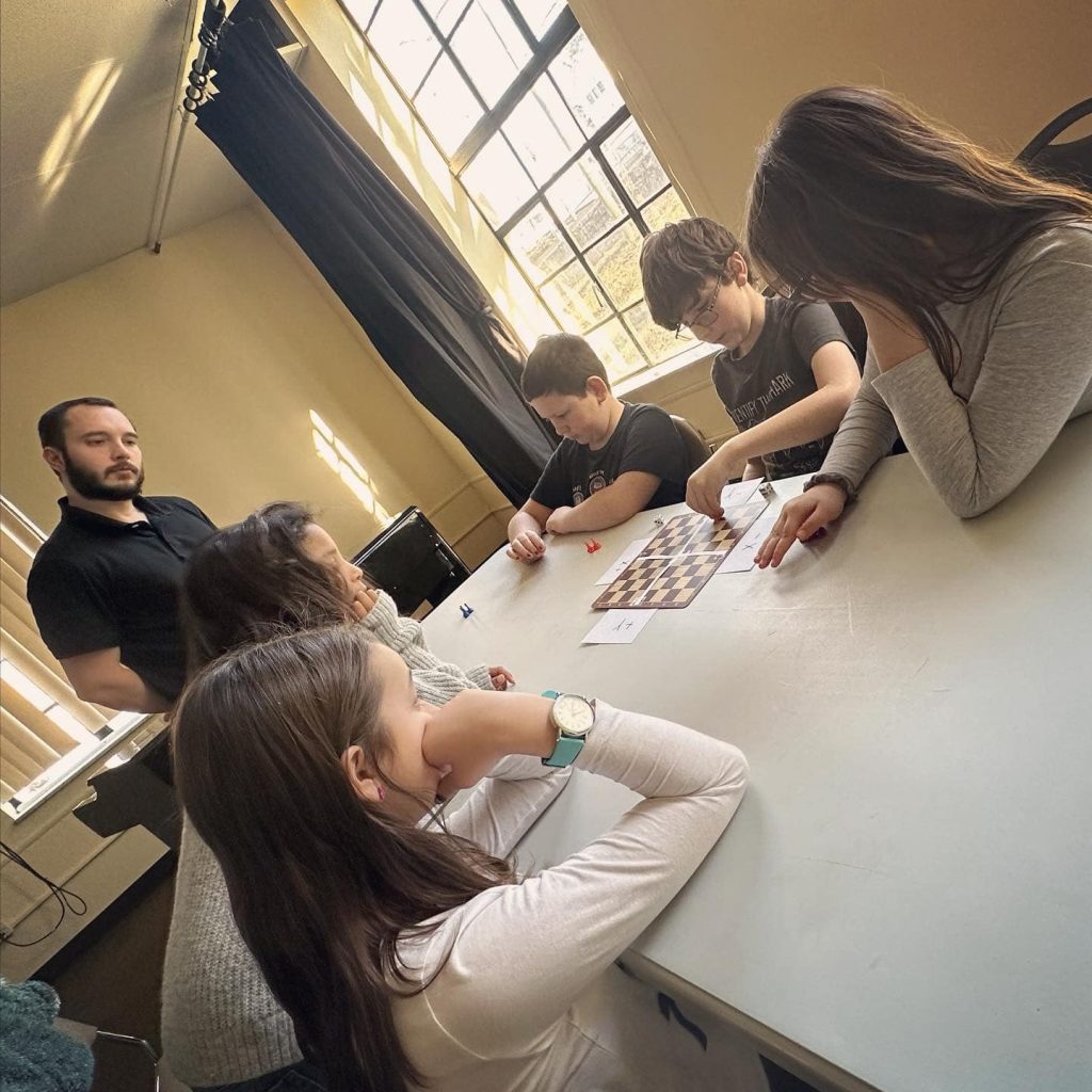 Students and a teacher gathered around a table working through a chess position.